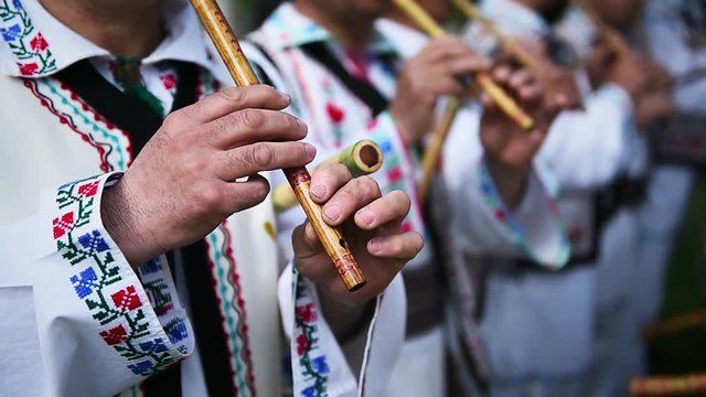 People in romanian traditional costumes singing at wooden flutes