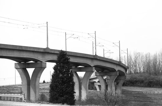 Fototapeta A curving concrete overpass bridge with cement pillars in black and white