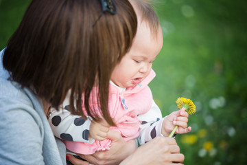 Mother holding her one year old sad baby girl, who has a dandelion in her hand; baby's face is sad and showing discomfort