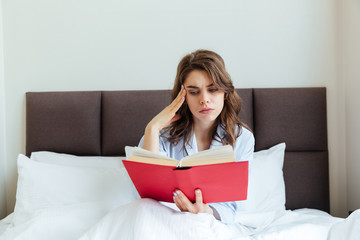 Portrait of a thoughtful young woman in pajamas reading book