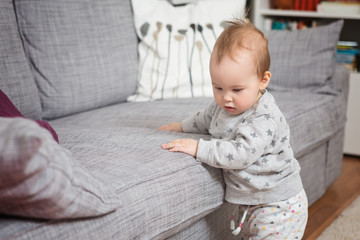 Fototapeta premium Eleven months old baby girl standing by the sofa