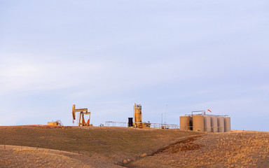 Oil pump and holding tanks surrounded by fenced pasture in a rolling hills spring Montana landscape