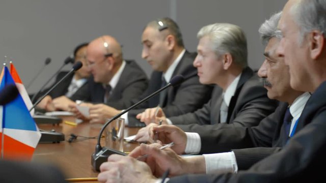 Mixed ethnicity business or politics group of delegates from different countries listen a speech and applaud the speaker at professional economic business conference. Political debates at round table