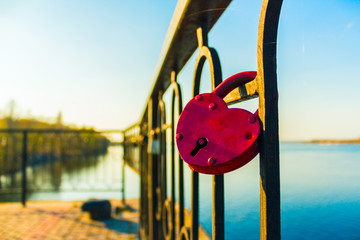 Red padlock of the heart shape on the fence of a river wharf