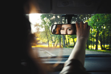 Reflection of a cheerful beautiful girl in a mirror of a car