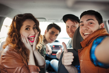 A company of four friends makes selfie inside the car