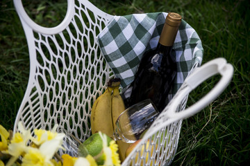 White plastic basket for eating or picnic. With wine, glasses, fruit and yellow flowers inside