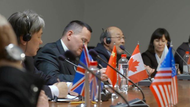 Two asian participants of international economic summit friendly discuss a question at round table. Diverse politicians from many contries of the world take part in multinational meeting or forum in