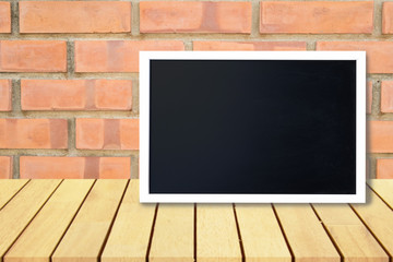 Blank black chalkboard lean on wooden table and brick wall,  Blank copyspace for your text or design.