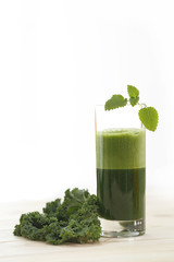 Green vegetable juice in a tall glass with a leaf of kale and mint