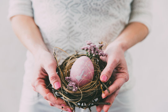 Hands holding modern painted easter egg in a small nest