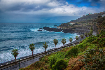 Old road along the ocean, waves, palm trees and mountains on Madeira Island, Portugal.