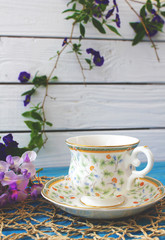 A cup of tea on a wooden blue table with a bouquet of colored field flowers