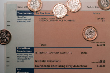 Personal income statement showing income and tax figures  for UK tax return covered by some new one pound coins