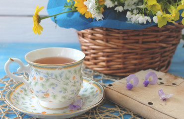 A cup of tea on a wooden blue table with a bouquet of colored field flowers