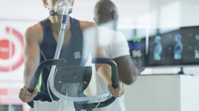  Male athlete on exercise bike being tested and monitored by sports scientist. 
