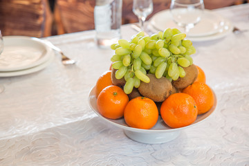 Plate with fruits oranges, grapes, kiwi with empty glasses and flatware on the background