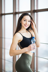 Fototapeta na wymiar beautiful girl standing in the gym with bottle of water at the window