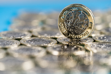 new pound coin introduced in Britain in 2017, front, standing on a layer of coins and on a blue background