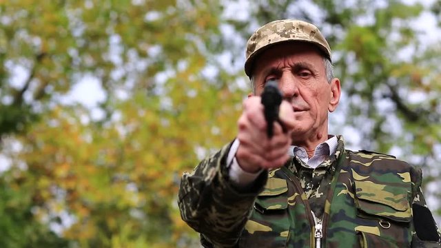 Retired officer in military uniform at shooting range. Senior man holds in hand black revolver and looks at the camera