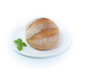 Full rustic loaf bread with basil leaves on a white dish isolated on white background