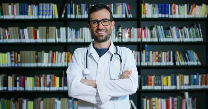 A young and beautiful female doctor in a library smiling happy and holding books after doing a search and after studying. Concept: educational, portrait, library, and medical care and welfare