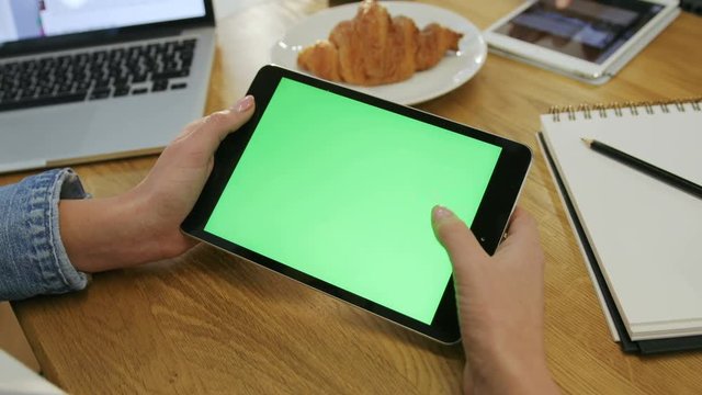 Woman hands using digital tablet touchscreen device with green screen in cafe. Woman scrolling photos, news, pages on tablet computer. Close-up. Chroma key