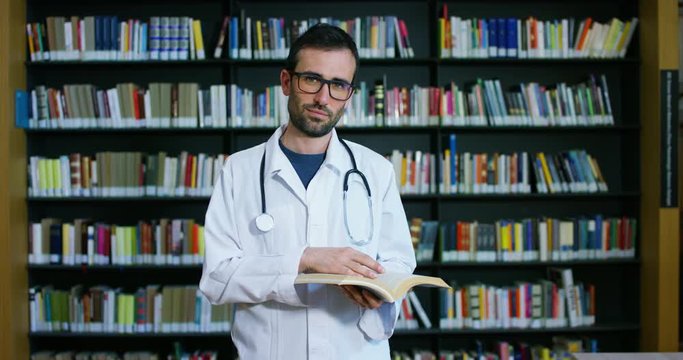 A young and beautiful female doctor in a library smiling happy and holding books after doing a search and after studying. Concept: educational, portrait, library, and medical care and welfare