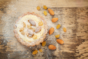 Delicious crispy tart with sugar powder, almond and raisins on wooden table