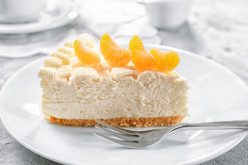 Piece of delicious cheesecake with tangerine on white plate