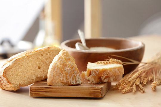 Tasty bread, wheat spikelets and wooden board on kitchen table