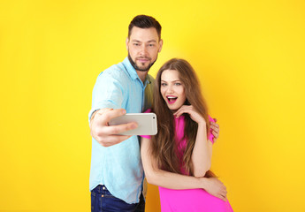 Fototapeta premium Happy young couple taking selfie on color background