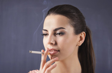 Obraz premium Young woman smoking cigarette on dark background