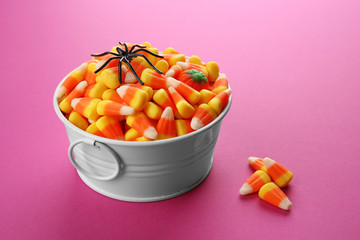 Bucket with tasty Halloween candies on color background