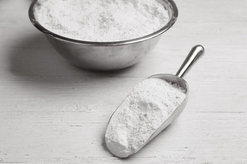 Bowl and scoop with flour on wooden table