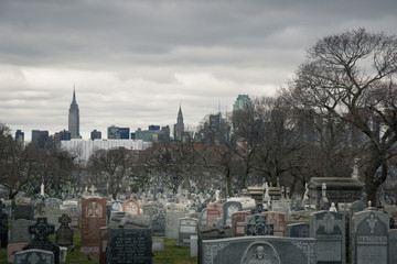 Calvary cemetery gravestones and trees on a dark cloudy day with Manhattan skyscrapers in the background - 143230063