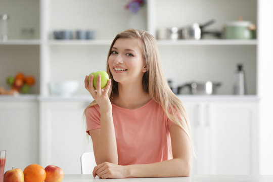 Young woman eating green apple at kitchen