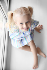 Cute little girl sitting on windowsill
