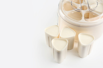 Cups and modern yogurt maker on white background