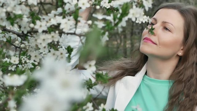 outdoor portrait of a beautiful woman in white jacket among white blossom tree