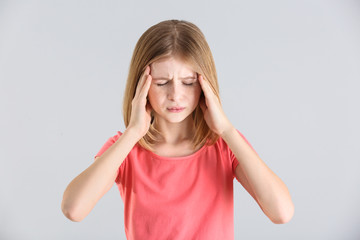 Cute girl suffering from headache on light background