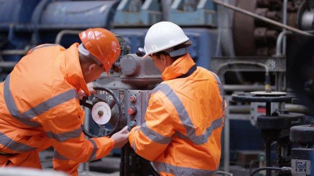  Male & female engineers in power plant turning a valve on machinery
