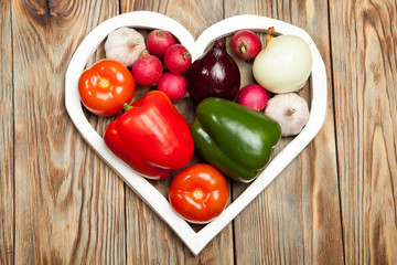 Vegetables. Peppers, tomatoes, garlic, onions, and radishes in the heart on rustic background