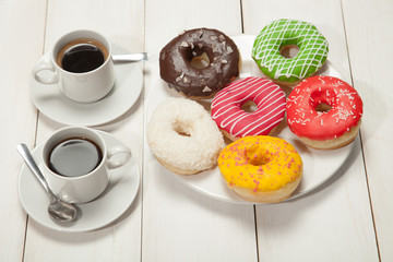 Two cups with coffee and donuts on a white wooden table