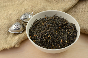 Loose jasmine dried tea leaves and flowers in white bowl with two tea infuser ball strawberries