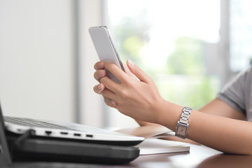 Young woman working at home using smart phone and notebook computer