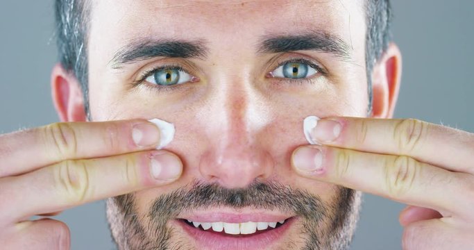 A very handsome man smiles and puts the face cream and eye contour anti-wrinkle and anti-aging for the care of his body and knows beauty. Concept: beauty, cream, beauty