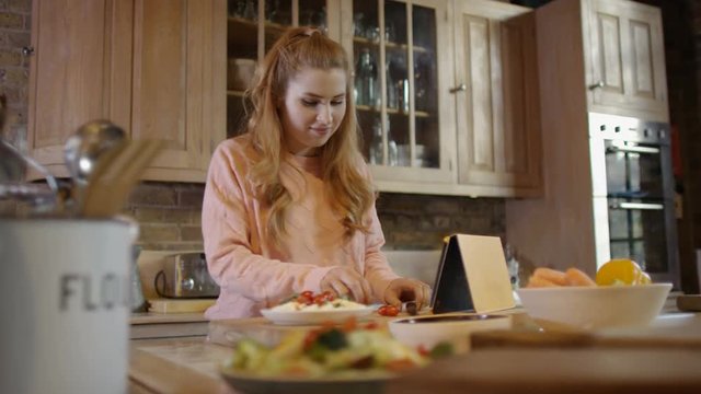  Young woman preparing meal in kitchen at home & following recipe on computer 
