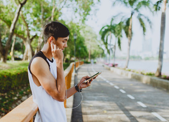 Attractive young sportsman listening to music from smartphone at public park.