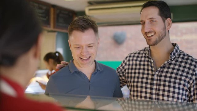  Gay male couple in a bakery shop making contactless payment by cell phone